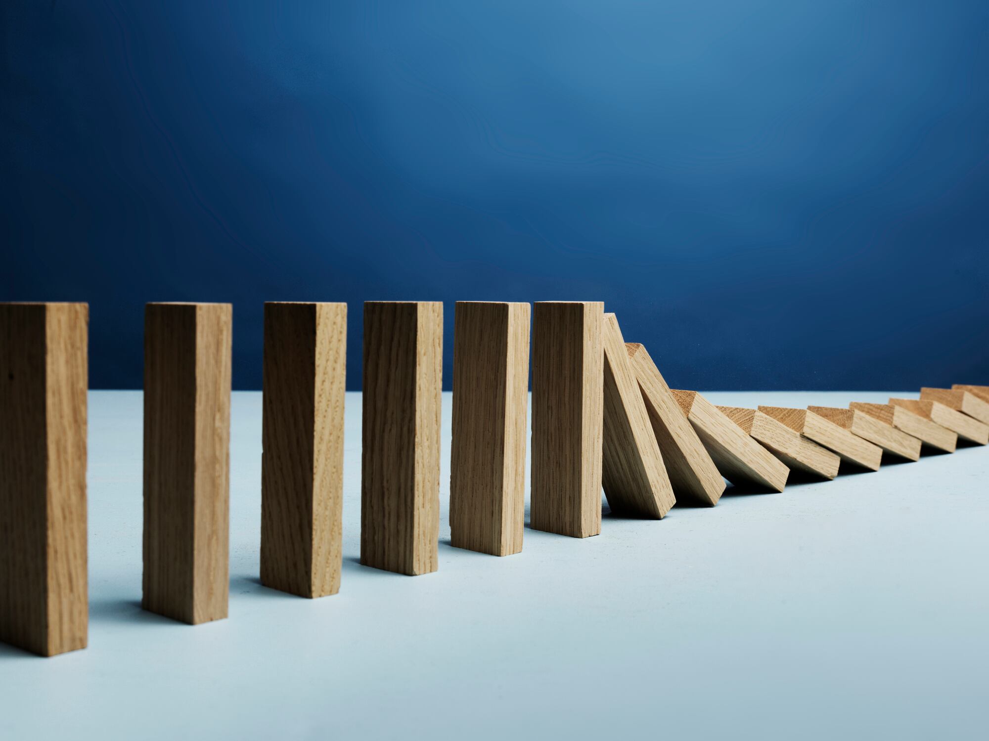 wooden blocks falling over, domino effect, photographed on blue background