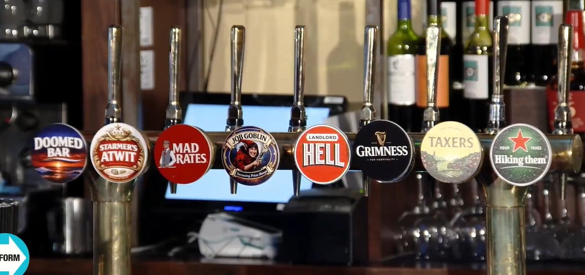 Satirical tap badges displayed during Reform UK’s Facebook Live press conference