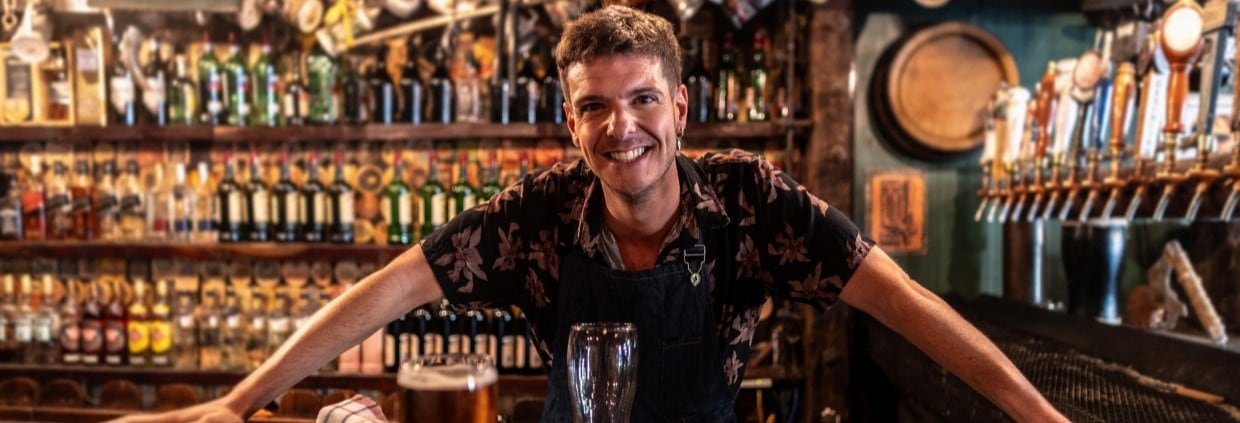 Barman standing behind pub bar with pint