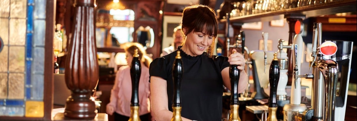 Pub landlady pulling pint behind the bar