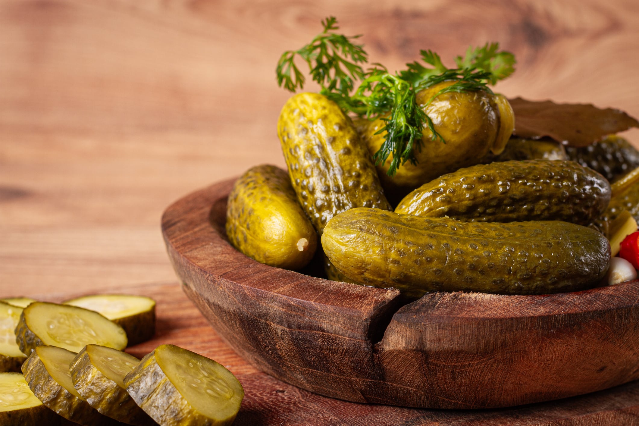 Pickled cucumbers in a wooden bowl with herbs and spices, close-up, rustic style,