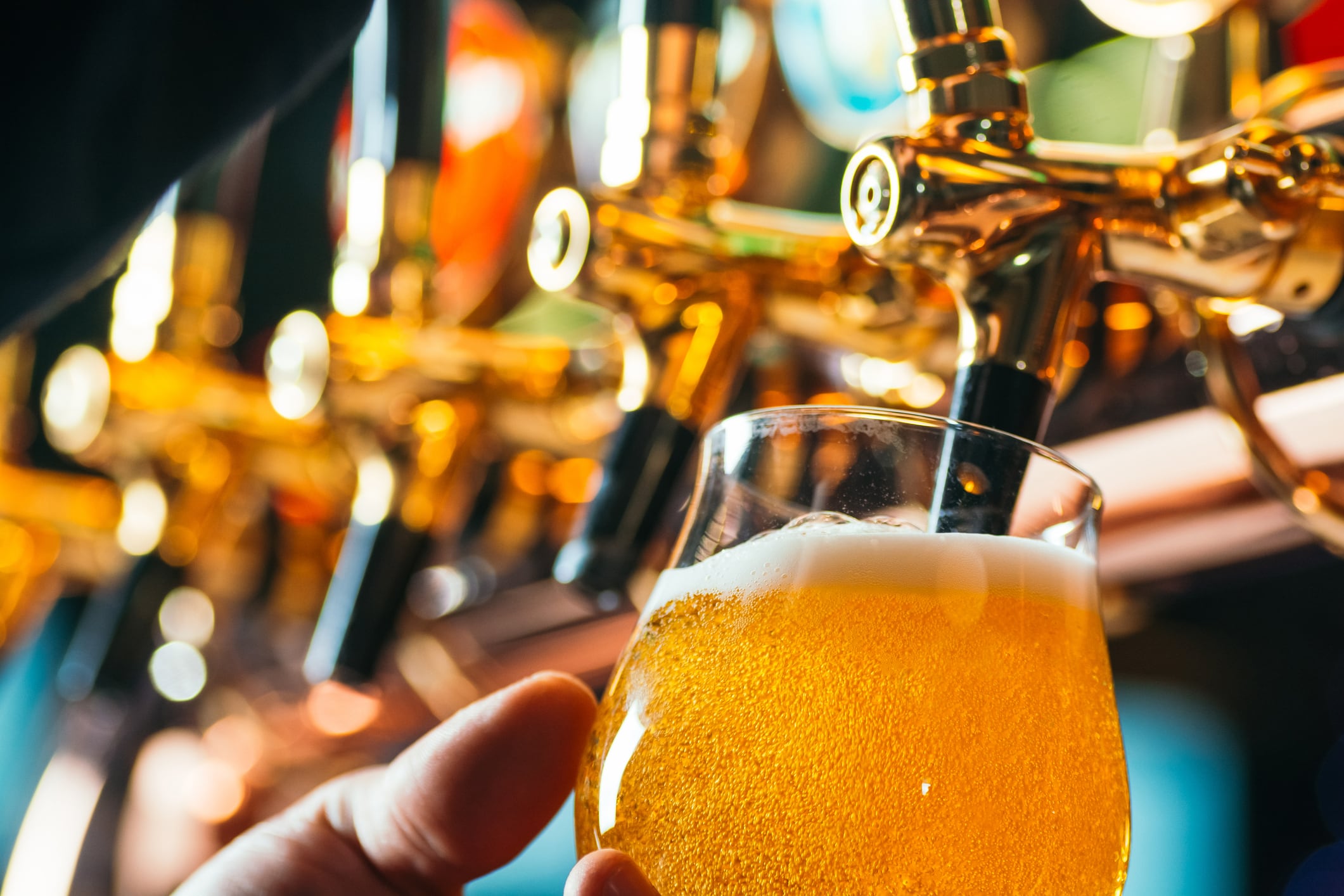Close up of bartender pouring fresh craft beer into a glass from beer taps in a pub