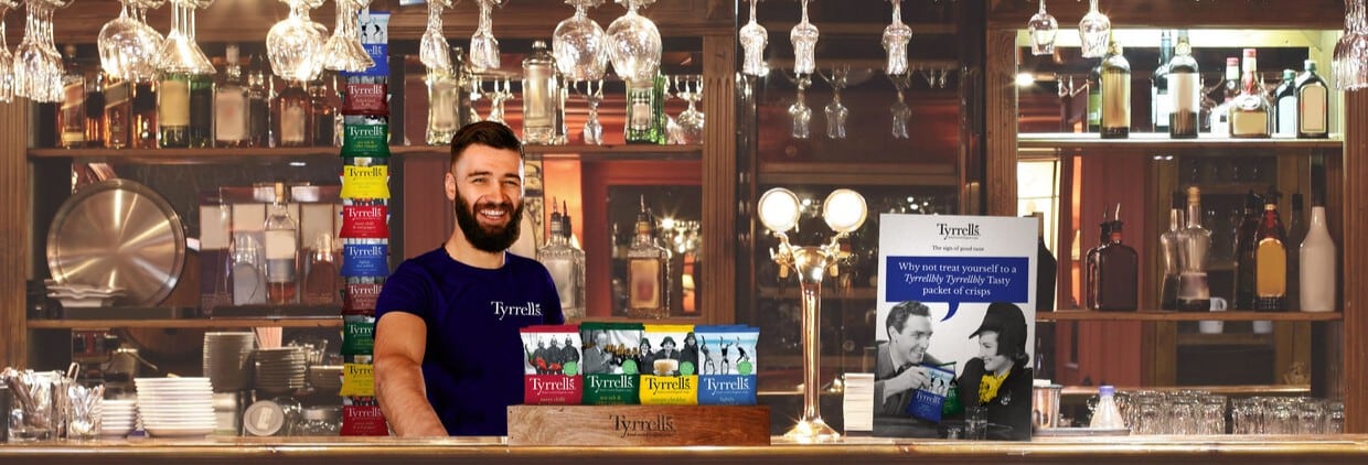 Bar staff behind bar with Tyrrells crisps