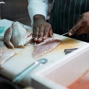 A close up of a chef filleting fish in a kitchen